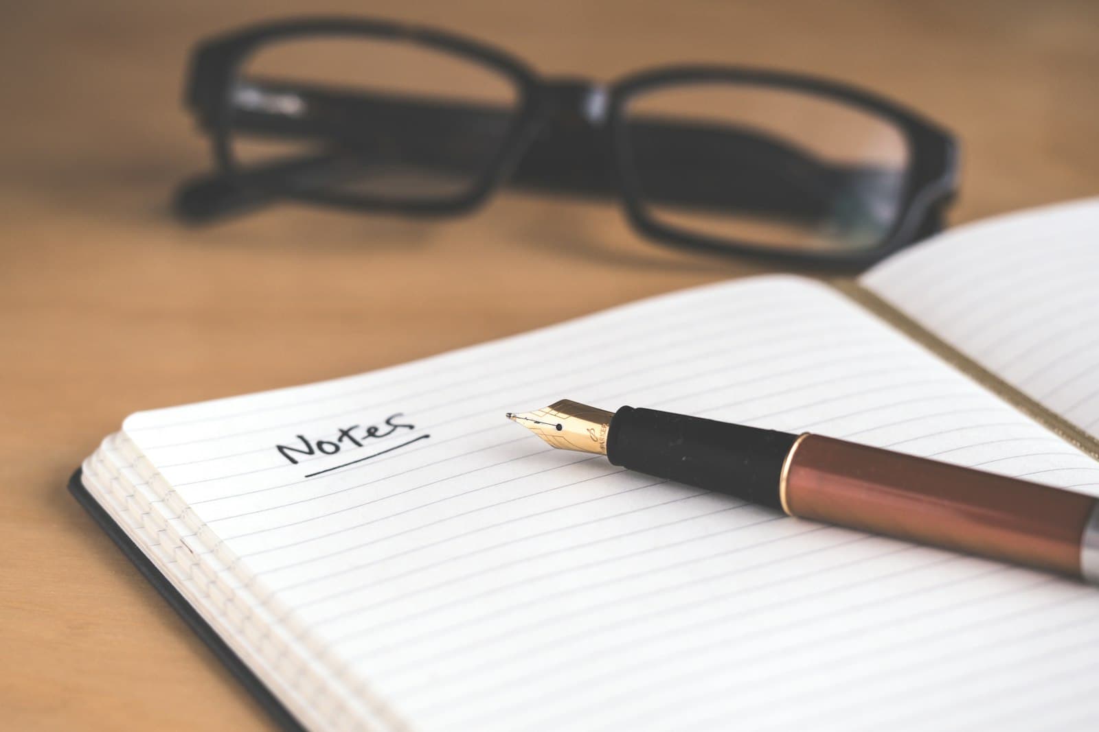 An open notebook titled Notes with a fountain pen resting on it and reading glasses nearby